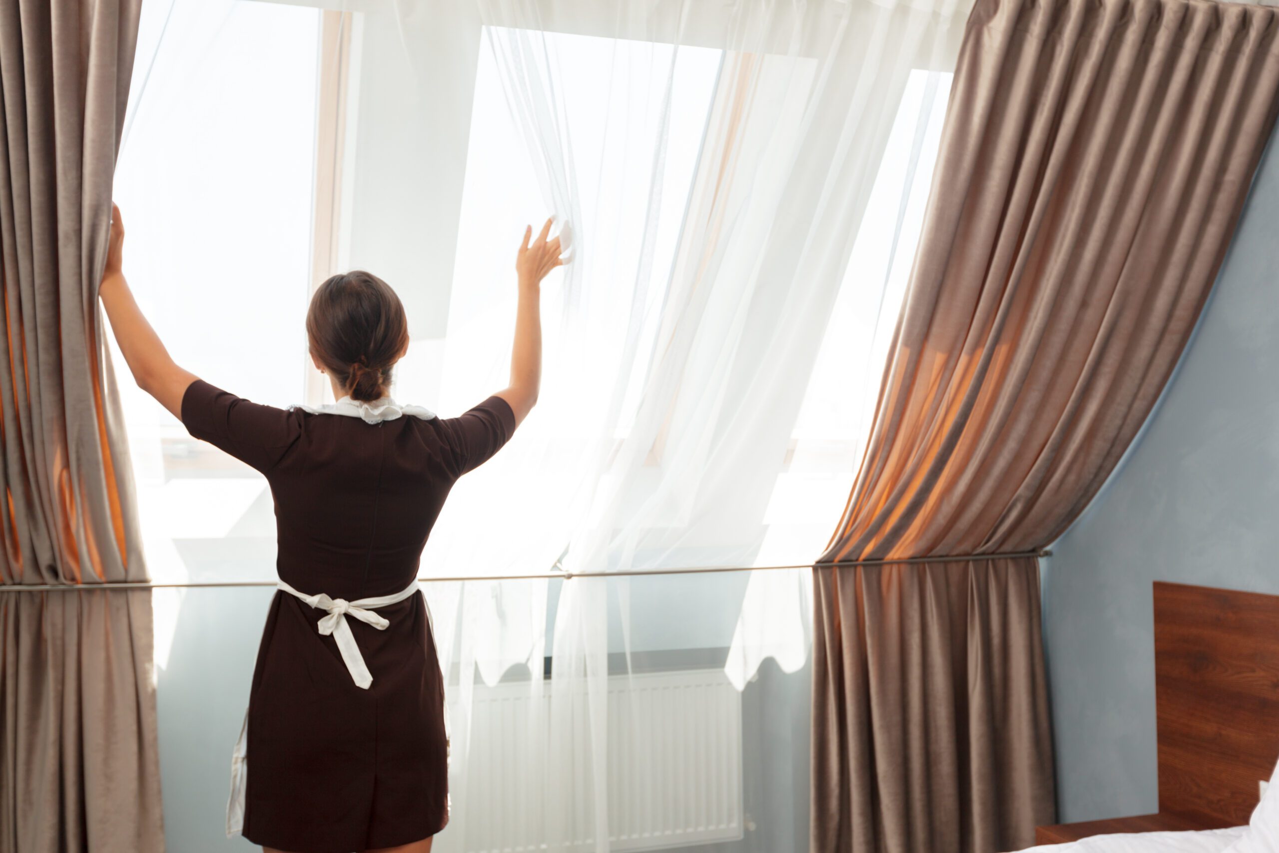 Hotel service concept. Chambermaid adjusting curtains in the room