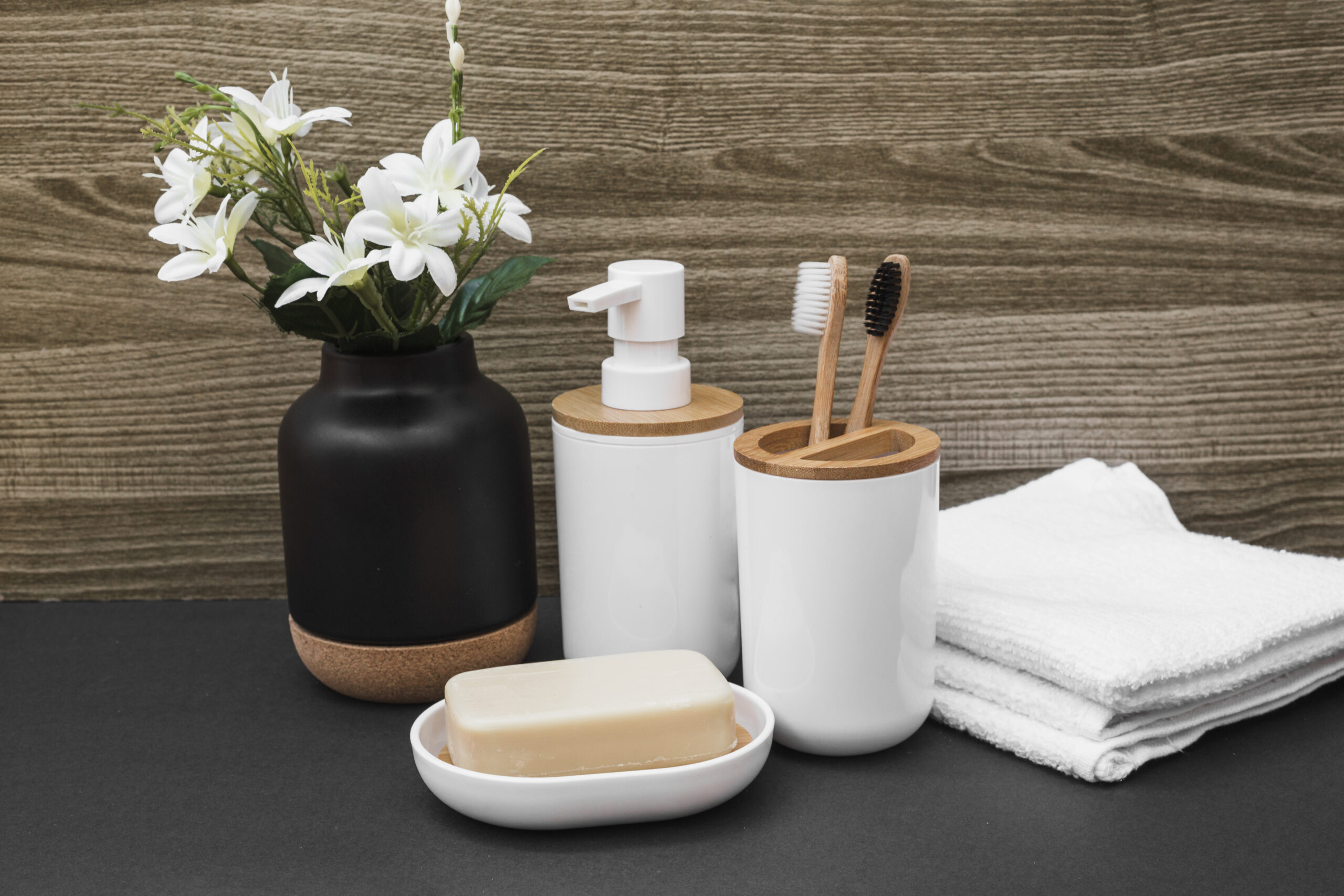 soap-toothbrush-cosmetic-bottle-towel-white-flower-vase-black-surface