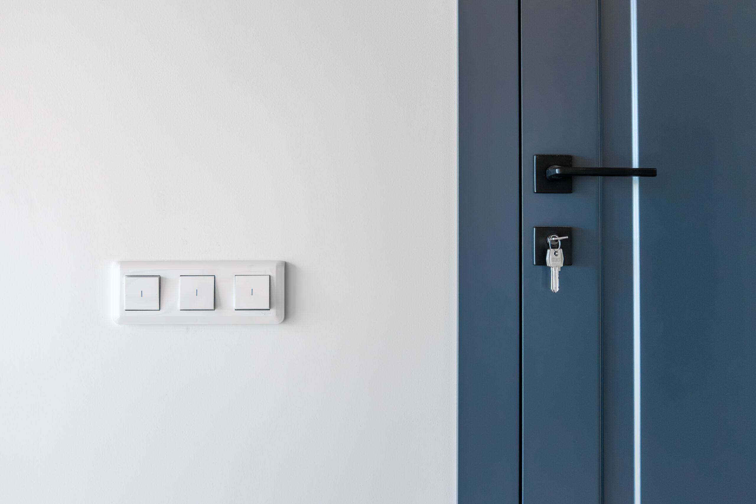 Bright wall switches beside a blue door with a black lock and key, clean lines and balanced contrast, a smart home detail in a minimalist scene.