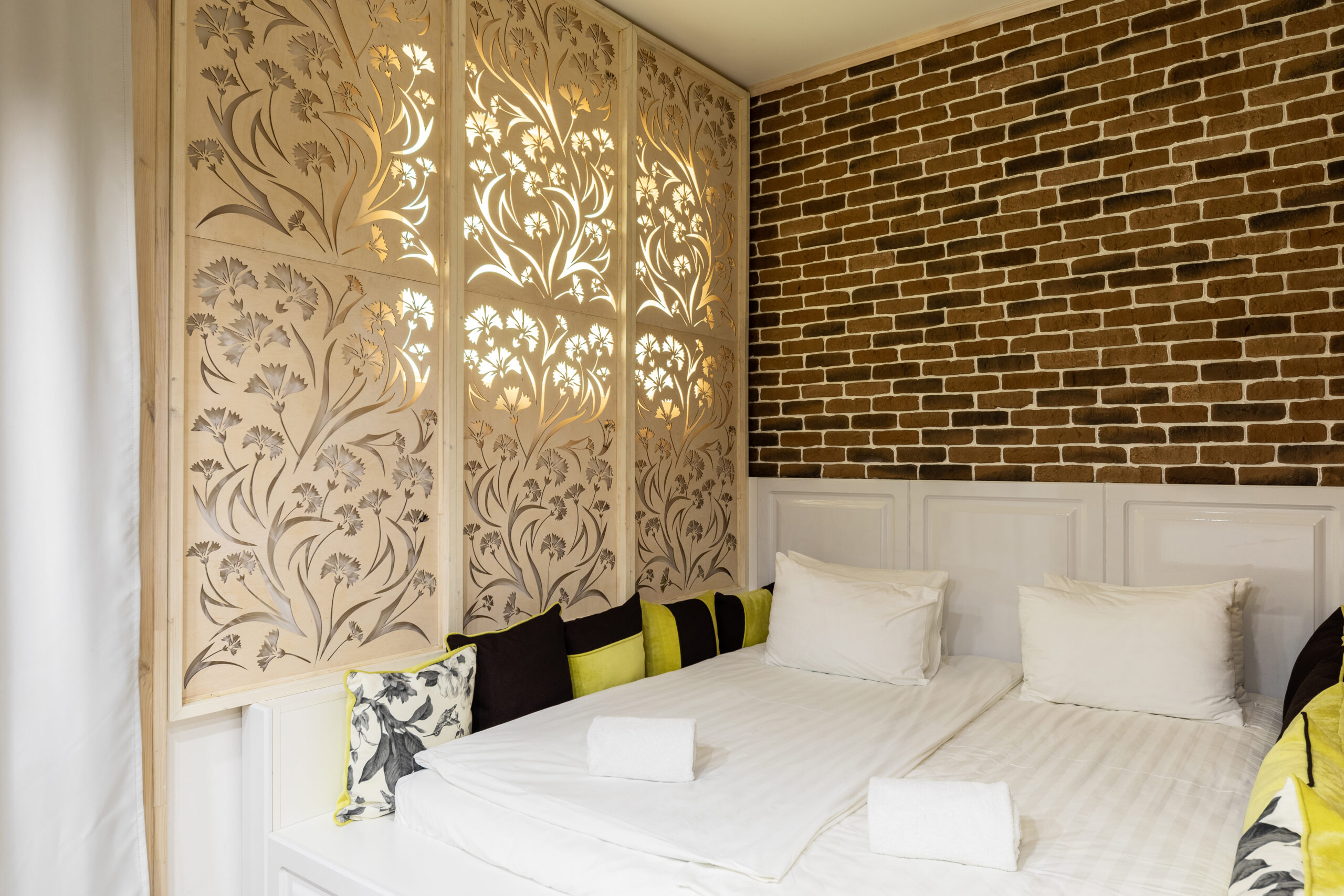 zoning space in the bedroom with a large double bed and a partition made of wood on which flowers are carved, at the headboard there is a wall of faux brick.
